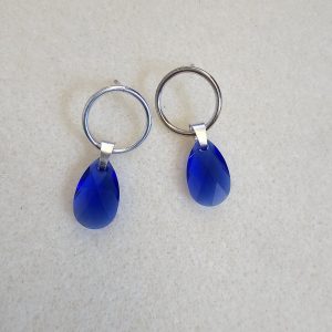Pendientes de plata hechos a mano con cristal azul facetado en forma de gota de 15 mm sobre fondo claro.